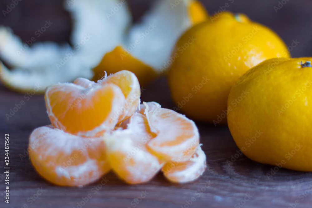 peeled tangerine slices and whole tangerines on wooden background
