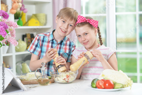 Cute brother and sister spicing salad at home