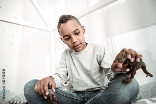 Dinosaur age. Pleasant young boy holding a dinosaur toy while playing with it © zinkevych