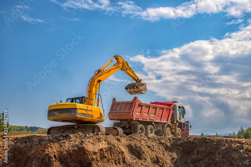 Yellow excavator and empty dump truck working at the construction site
