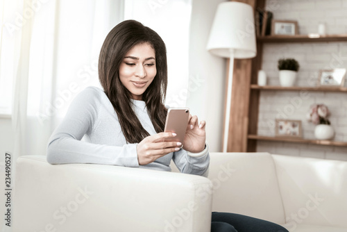 International beauty. Charming longhaired female keeping smile on her face while staring at smartphone