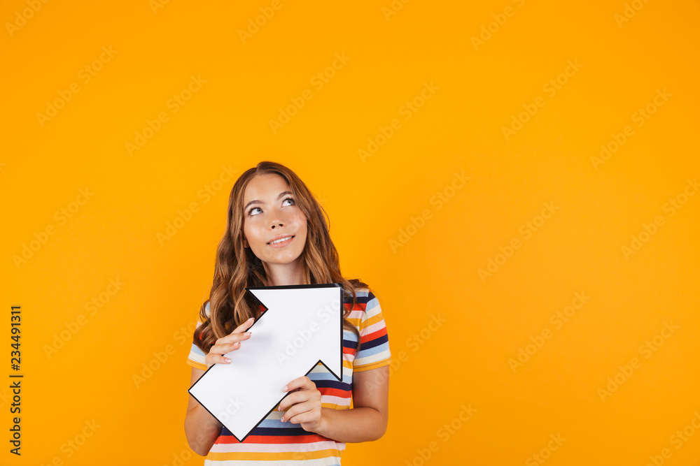 Beautiful girl posing isolated over yellow background holding arrow. Beautiful girl posing isolated over yellow background holding arrow.