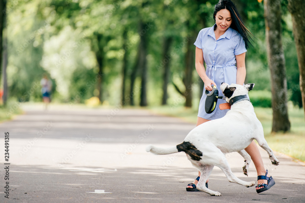 Obraz premium Happy cheerful smiling brunette girl in blue summer dress playing with big hunting dog in park. Beautiful young woman training her active funny puppy outdoor. Cute teen loves animals. Breeding pet