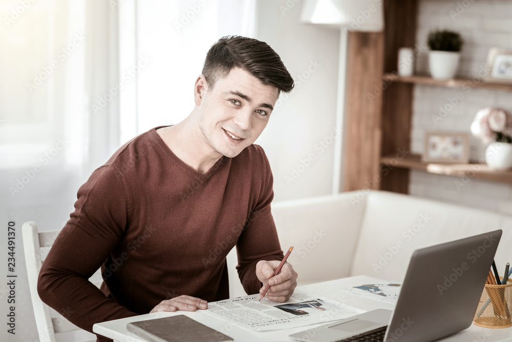 Fototapeta premium Have idea. Kind young man keeping smile on his face while sitting at his workplace