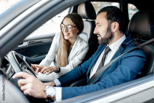 Businessman and woman dressed in the suits talking together while driving a luxury car in the city