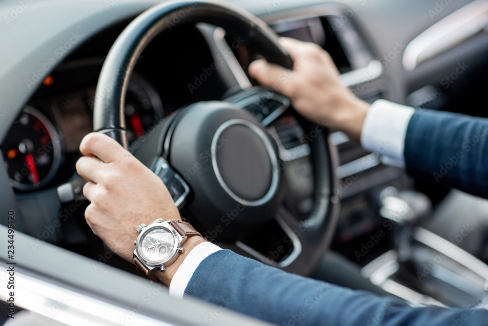 Close-up of businessman's hands on the helm of a luxury car