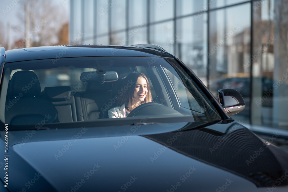 Young businesswoman driving a luxury car, view from the outside through the windshield