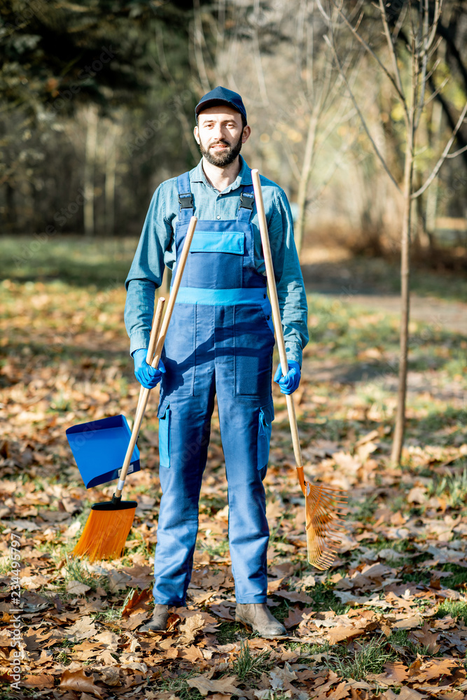 Portrait of a professional male sweeper in blue uniform with sweeping tools in the garden during the autumn time Portrait of a professional male sweeper in blue uniform with sweeping tools in the garden during the autumn time