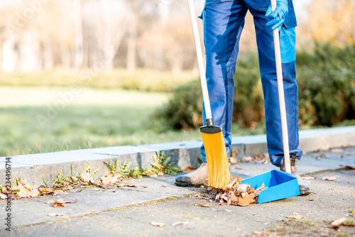 Man sweeping leaves with orange broom to the scoop on the street, close-up view with no face