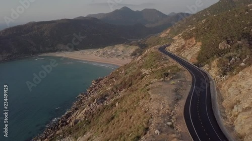2K Aerial view of beautiful Vietnamese landscape with curvy mountain road in the coastal seaside with the lonely beach and small lighthouse on the background. Phu Yen, Vietnam