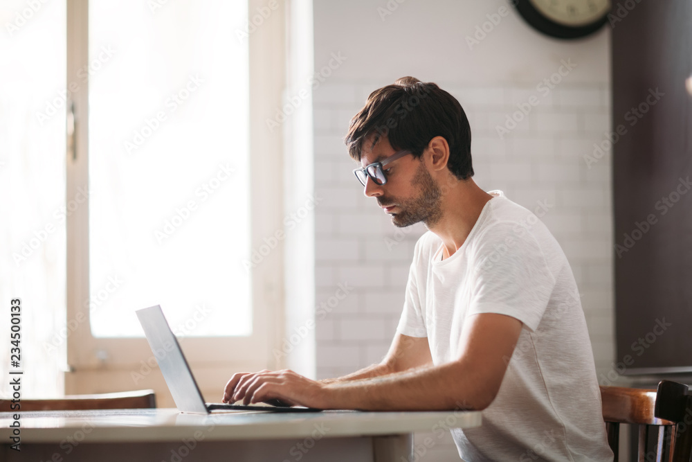 Young handsome man in glasses working on laptop in cozy interior Young handsome man in glasses working on laptop in cozy interior