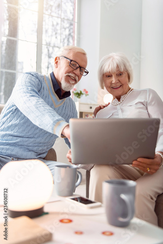 Online purchase. Aging beautiful couple smiling bright while eagerly discussing goods to be purchased online