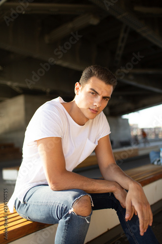 Caucasian boy in white t-shirt and ripped jeans sitting on the street