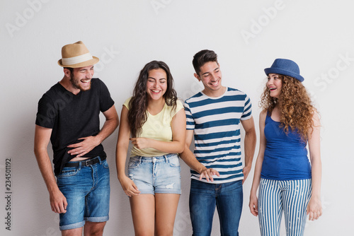 Portrait of joyful young group of friends with hats standing in a studio, laughing.