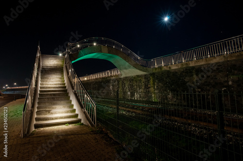 Colorful illuminated walkway inHarlingen with strap and metal silver balustrade in an organic curve shape.