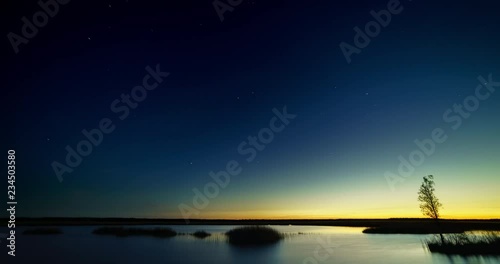 Night to day time lapse of stars over a lake with sunrise