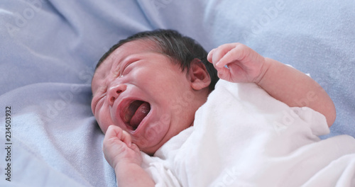 New born baby crying on bed