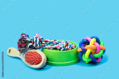 Pet accessories concept.  Brush, rubber toy and rope in bowls for pet on color background