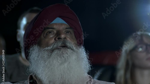 Indian man with large grey beard watching a movie photo