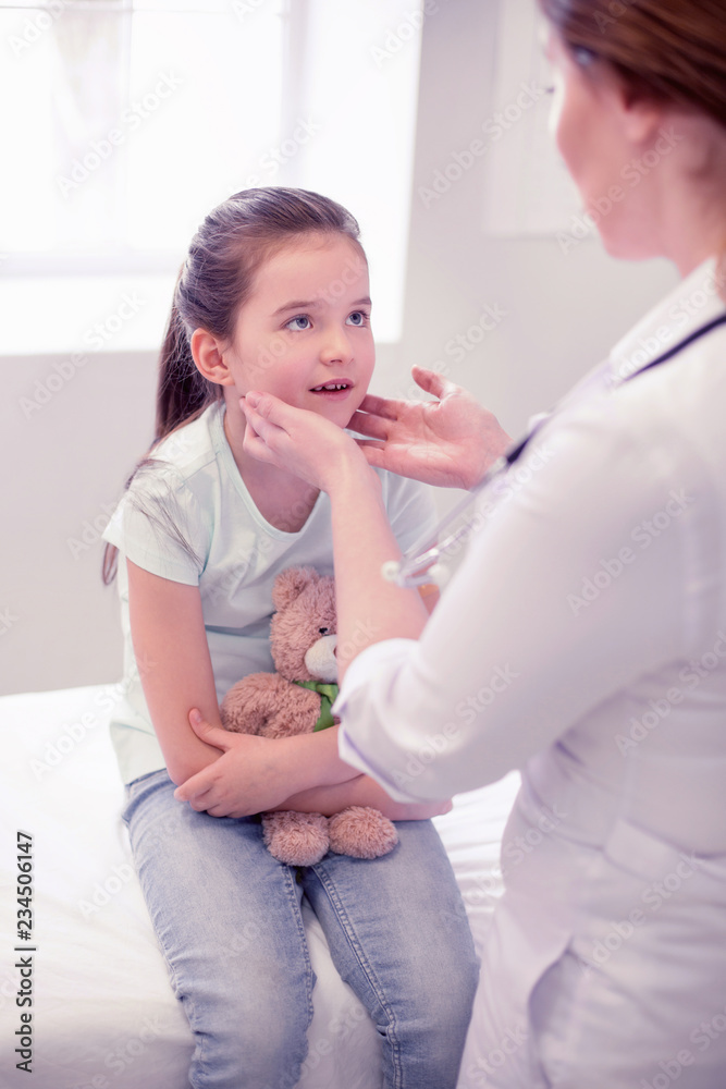 © zinkevych - Visiting doctor. Cute little preschool girl wearing jeans sitting with her toy while visiting doctor