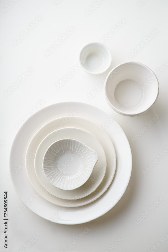Porcelain plates of various form and size on white background. Overhead image, copy space. Porcelain plates of various form and size on white background. Overhead image, copy space.