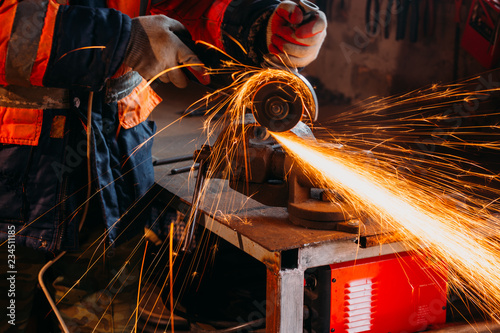 Fototapeta Worker cutting metal with grinder in his workshop