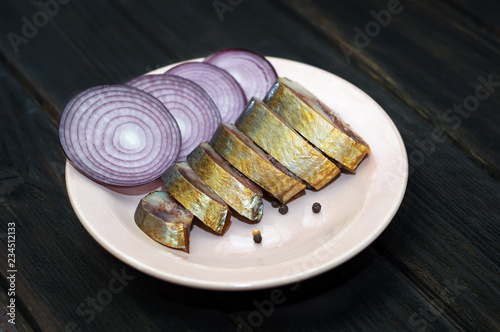 Smoked fish, cold smoked herring on a plate with onions, on a wooden table, gourmet snack.