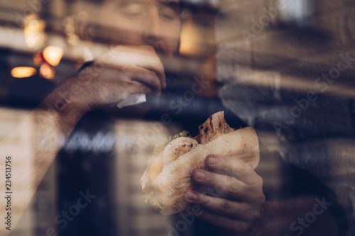 detail shot, man using his lunch break and eating a healthy chicken sandwich at a small restaurant, sitting next to the window. shot through the window, with city reflections