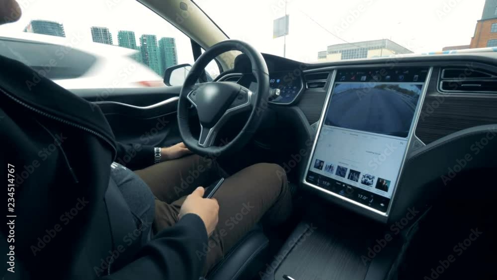 A man is sitting in a vehicle which is being automatically driven