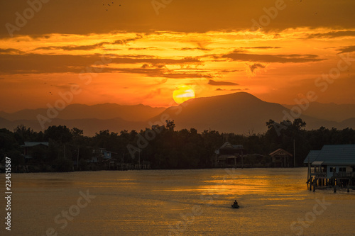 Sunset behind mountain.And the shadow of a riverside village and a fishing boat on the river.