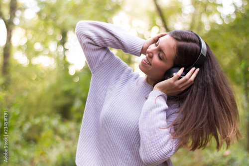 Caucasian european young woman or girl listening to music with helmets energetically and dancing moving her hair with energy in nature or very happy forest