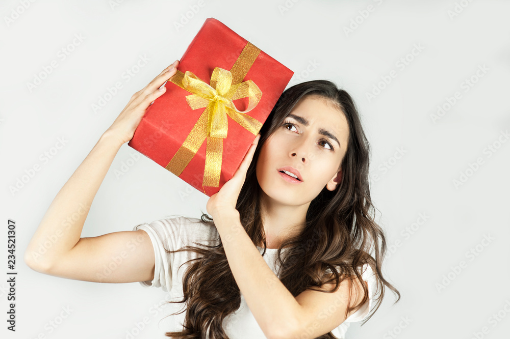 A young beautiful girl holds in her hands a big gift that keeps near the ear and listens to what is inside