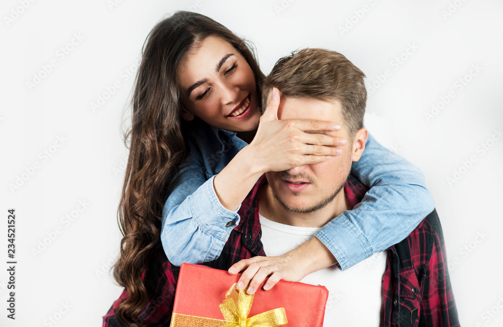 A young beautiful girl makes a surprise to her boyfriend and gives him a gift by covering his eyes with a hand. They laugh emotionally. A young beautiful girl makes a surprise to her boyfriend and gives him a gift by covering his eyes with a hand. They laugh emotionally.