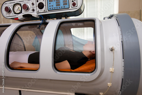 Treatment in an oxygen capsule. A beautiful girl in a black T-shirt and white pants is lying in a pressure chamber. The concept of modern medicine