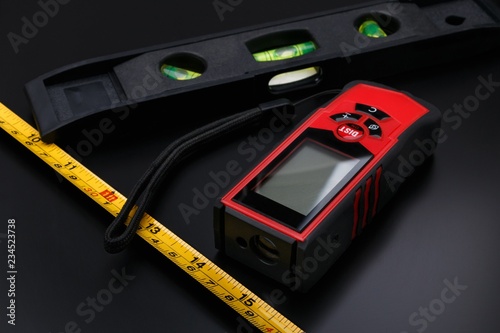 Tape measure, laser tape and building level on black matte surface photo