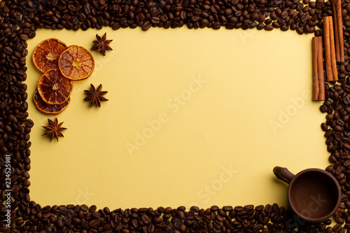 Conceptual coffee background. Yellow background, frame of coffee beans, slices of dried oranges and star anise. Beautiful clay cupin the corner of the frame. photo