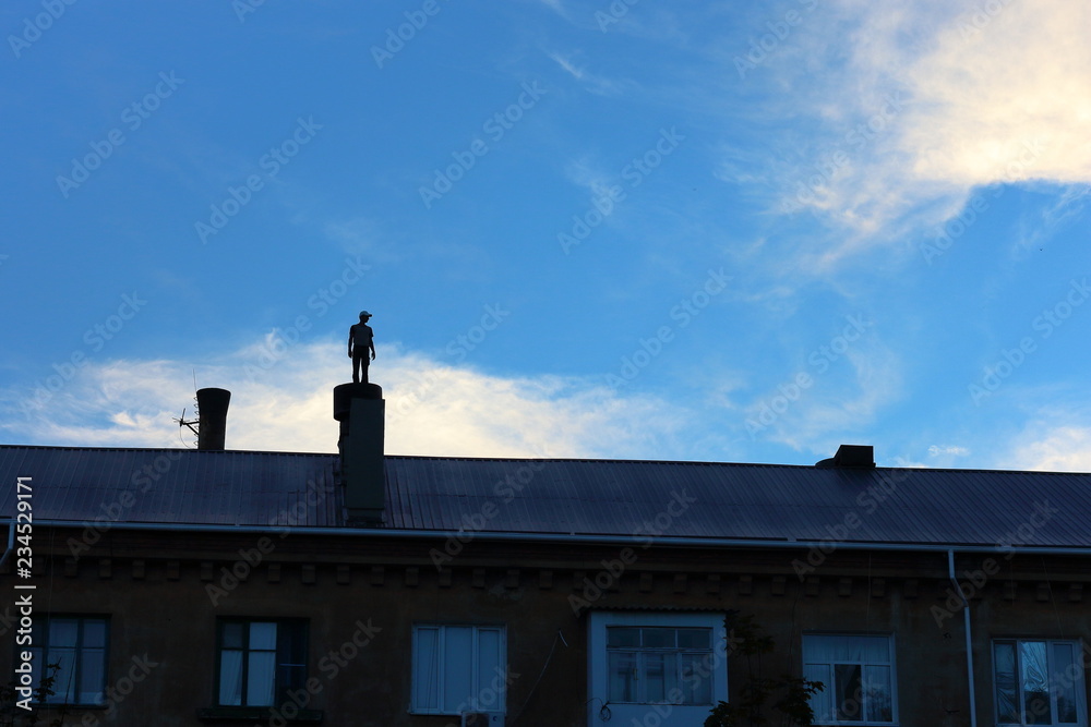 Silhouette of man standing on the chimney on the roof of the house against blue sky