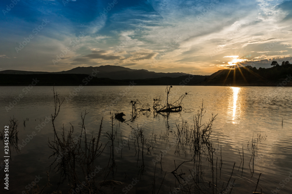 Landscape of unset reflected in the lake with sunbeams Landscape of unset reflected in the lake with sunbeams