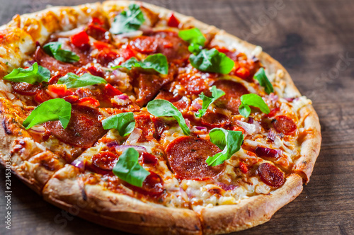 sliced Pepperoni Pizza with Mozzarella cheese, salami, chorizo, tomato sauce, pepper, Spices and Fresh arugula. Italian pizza on wooden table background