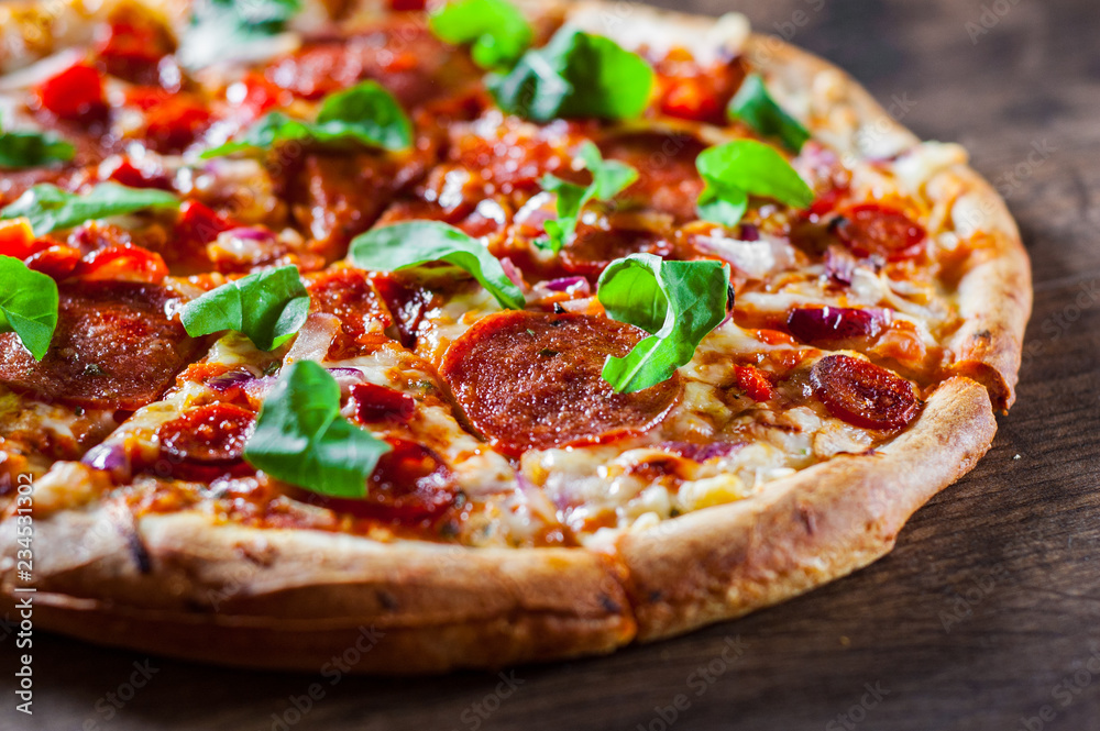 sliced Pepperoni Pizza with Mozzarella cheese, salami, chorizo, tomato sauce, pepper, Spices and Fresh arugula. Italian pizza on wooden table background