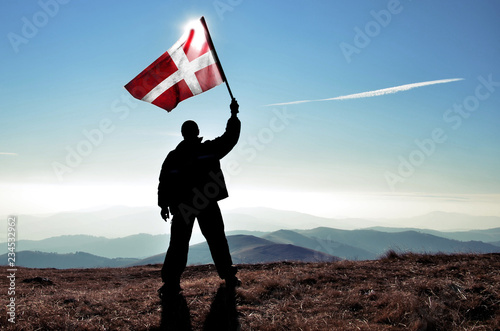 Successful silhouette man winner waving Denish flag on top of the mountain peak photo