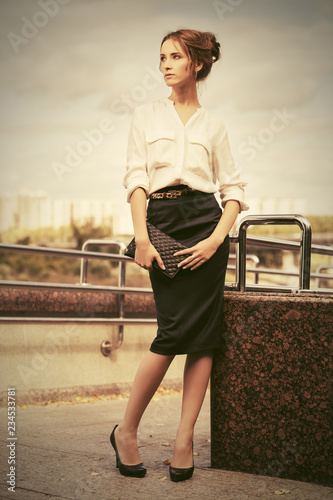 Young fashion business woman with handbag walking in city street