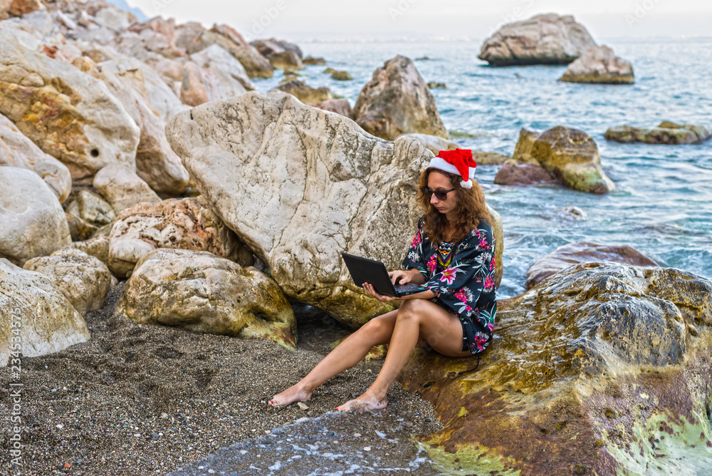 Workaholic young woman in a Santa hat working on the beach.
