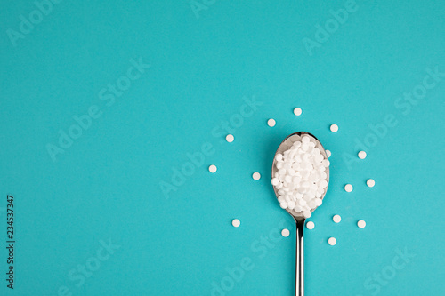 Foto Sugar substitute pills in a spoon, on a blue background