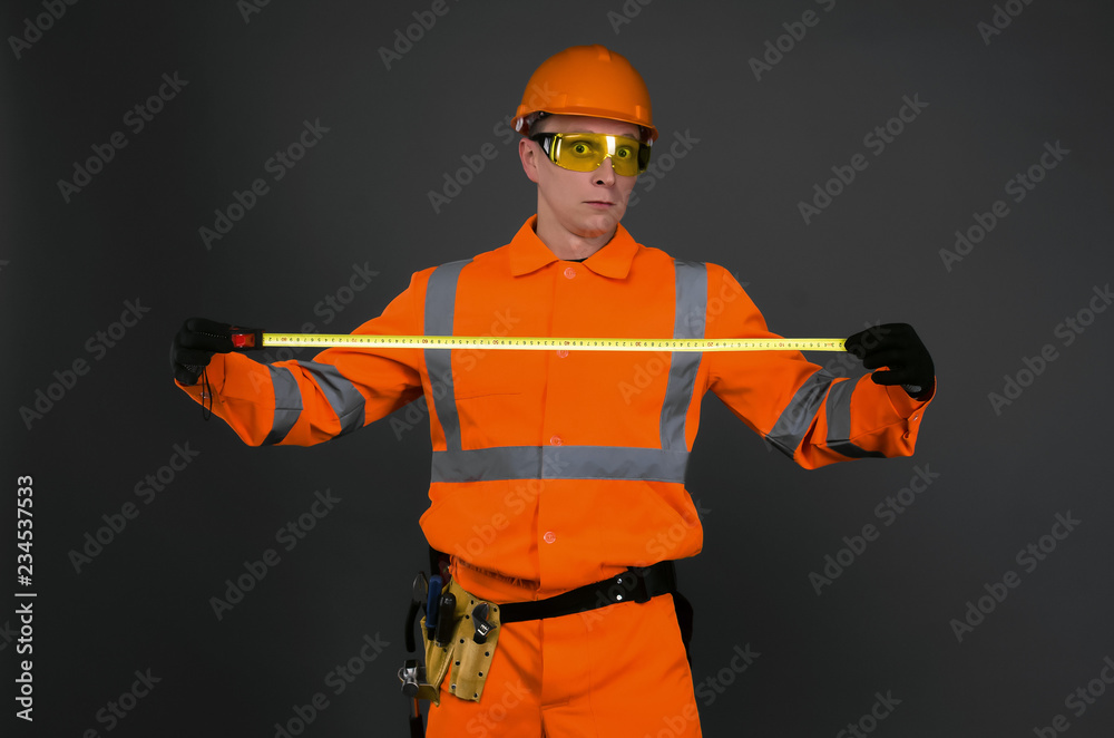 Fototapeta premium Shocked builder measurer with meter roulette in the hands surprised by the size isolated on gray background.