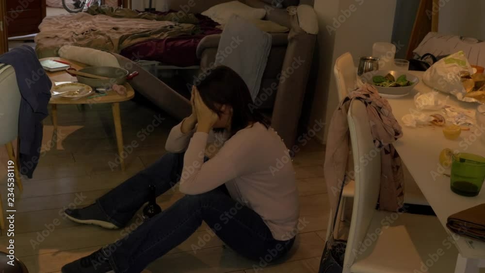 desperate  beautiful woman crying sitting on the flor of a messy house with a bottle of wine in front of her
