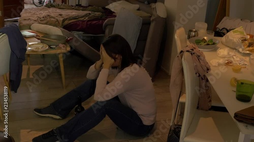 desperate  beautiful woman crying sitting on the flor of a messy house with a bottle of wine in front of her