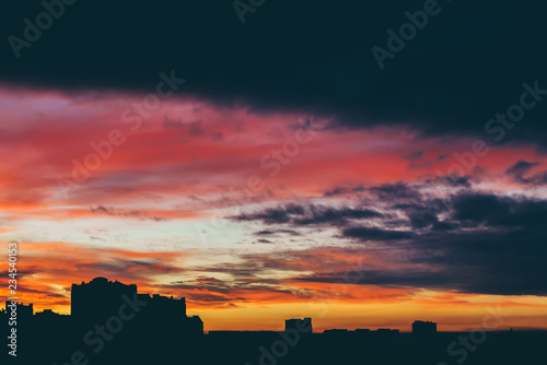 Cityscape with wonderful varicolored vivid dawn. Amazing dramatic multicolored cloudy sky above dark silhouettes of city buildings. Atmospheric background of sunrise in overcast weather. Copy space.