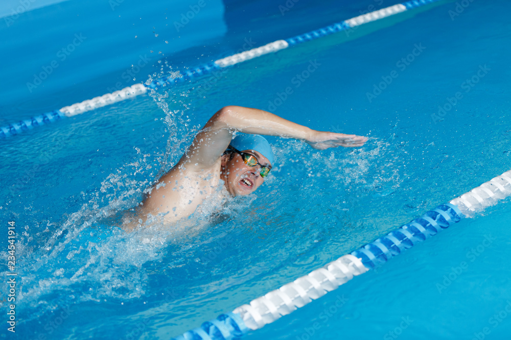 Photo of sportsman in blue cap swimming in style of crawl in swimming pool