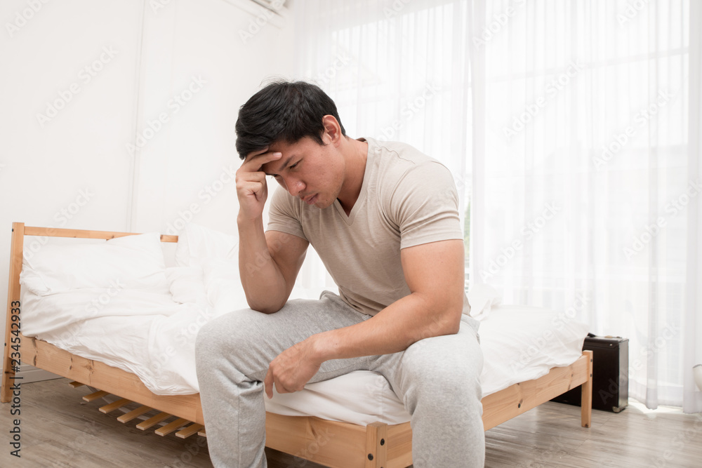 Asian man sitting on the bed and hand on forehead. Illness,stress,headache caused by overworking or hard work.